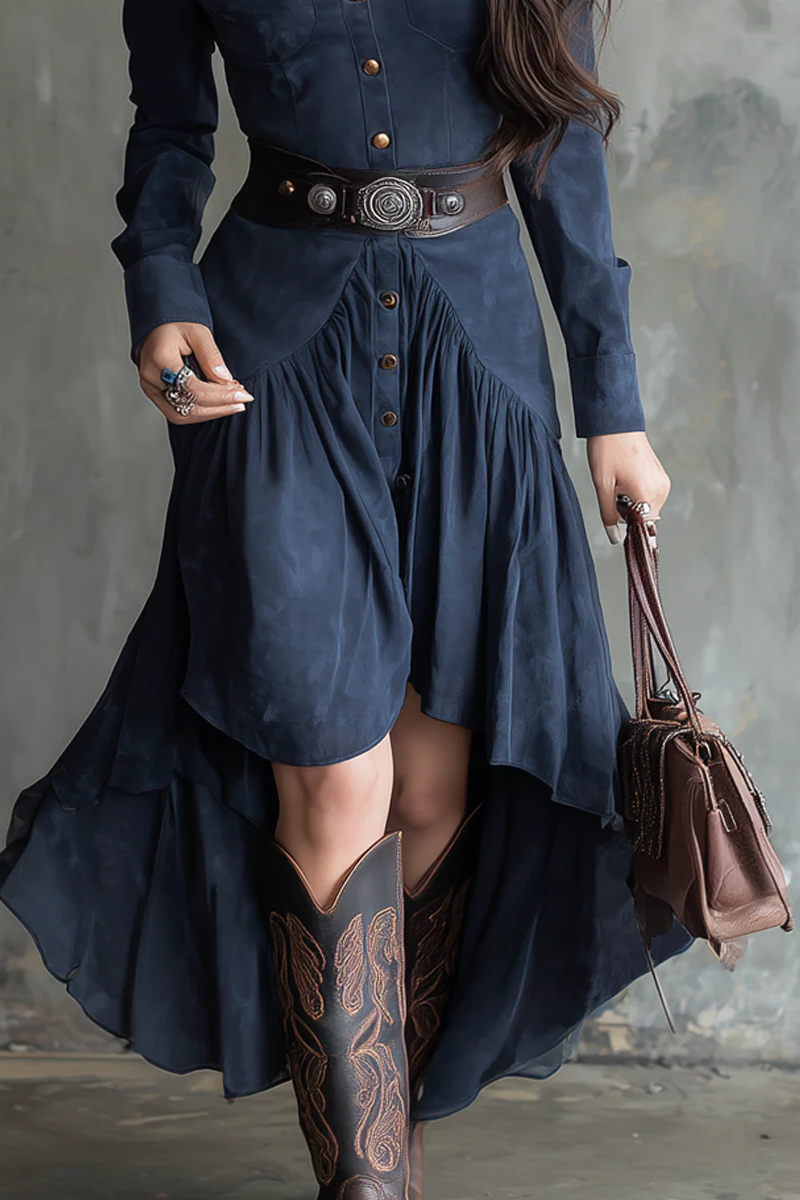 Person wearing a long navy dress with a belt and holding a brown leather bag against a gray background