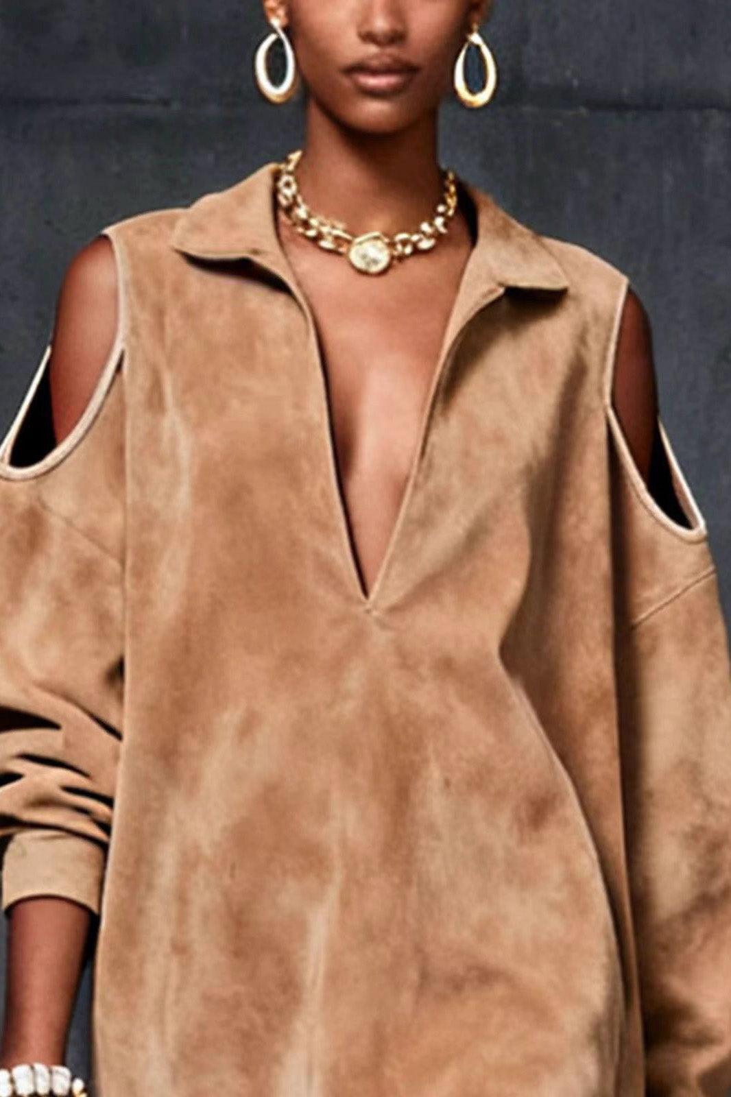 Woman wearing a brown suede dress with cut-out shoulders against a dark background