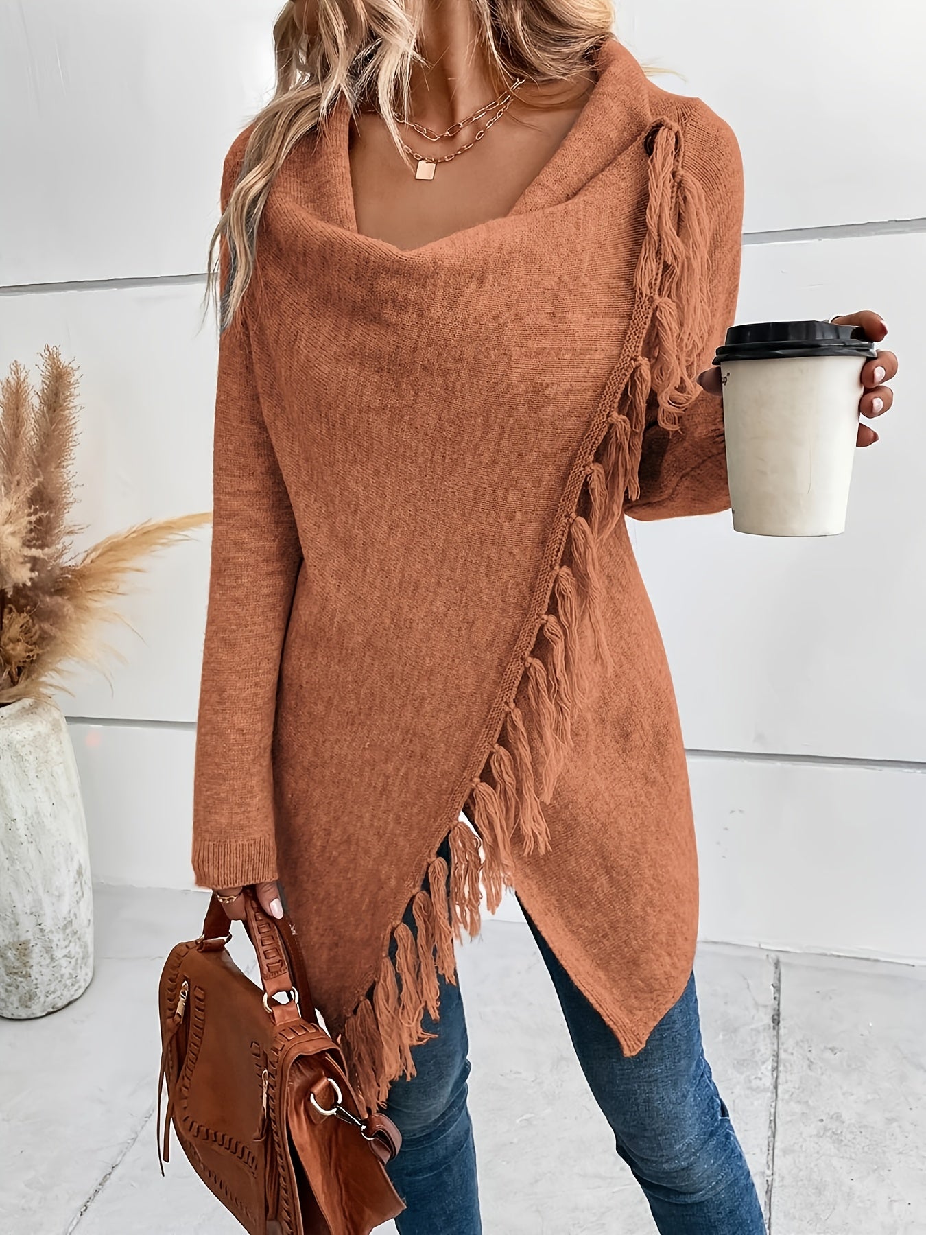 Person wearing a brown fringe sweater holding a coffee cup and a handbag.