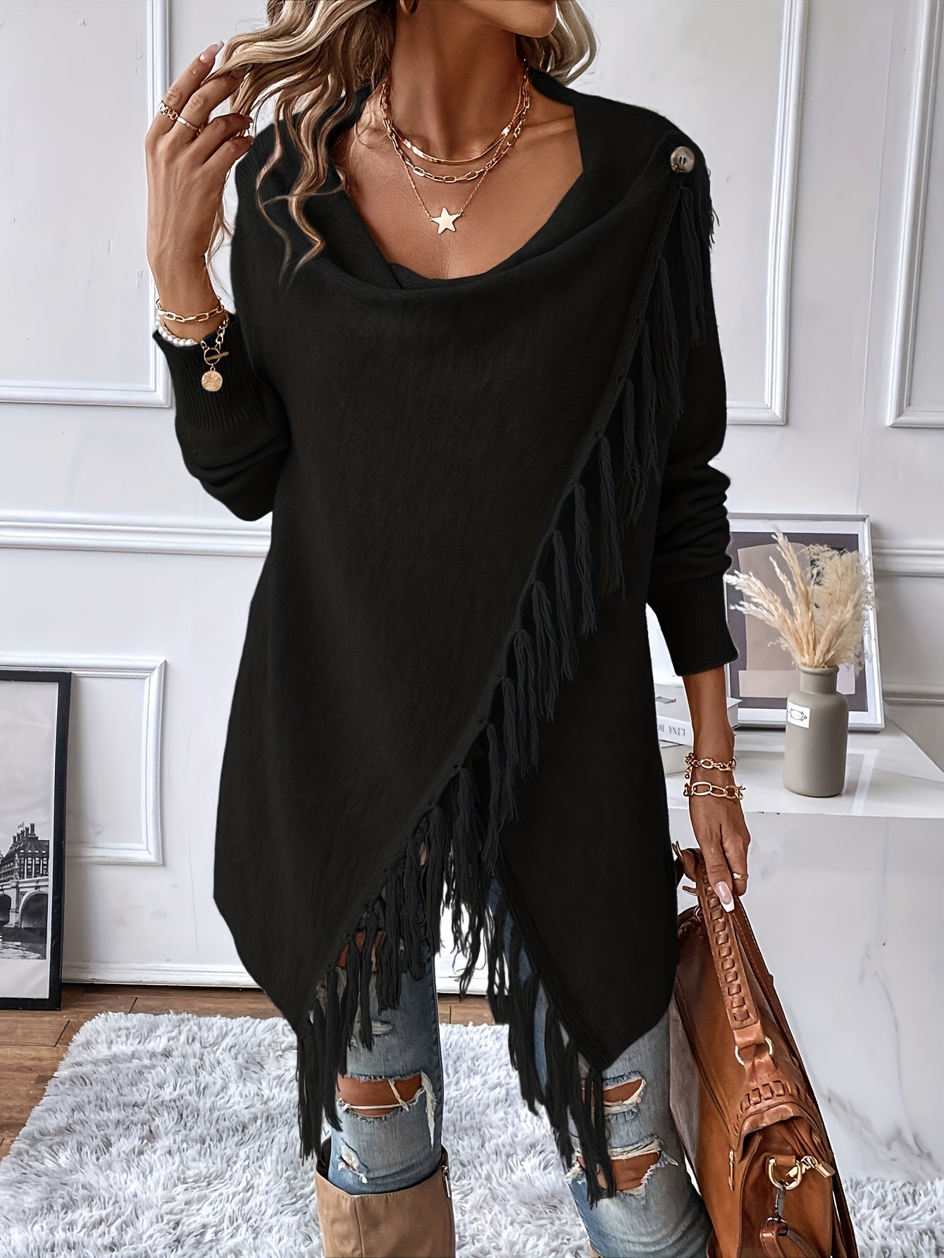 Person wearing a black fringe sweater with ripped jeans and holding a brown bag in an indoor setting.