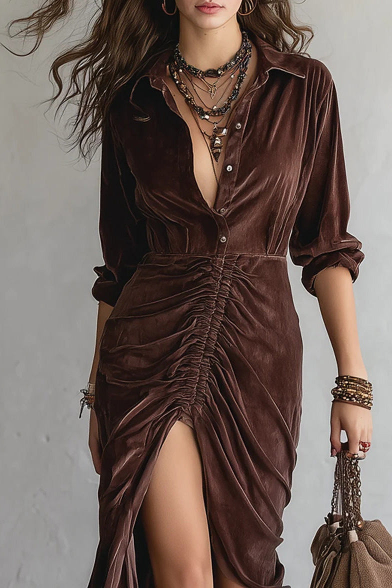 Woman wearing a brown velvet dress with a high slit, holding a matching handbag against a plain background.