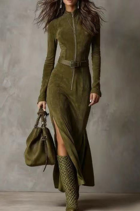 Woman wearing a green dress with a belt and high boots, holding a matching handbag against a neutral background.