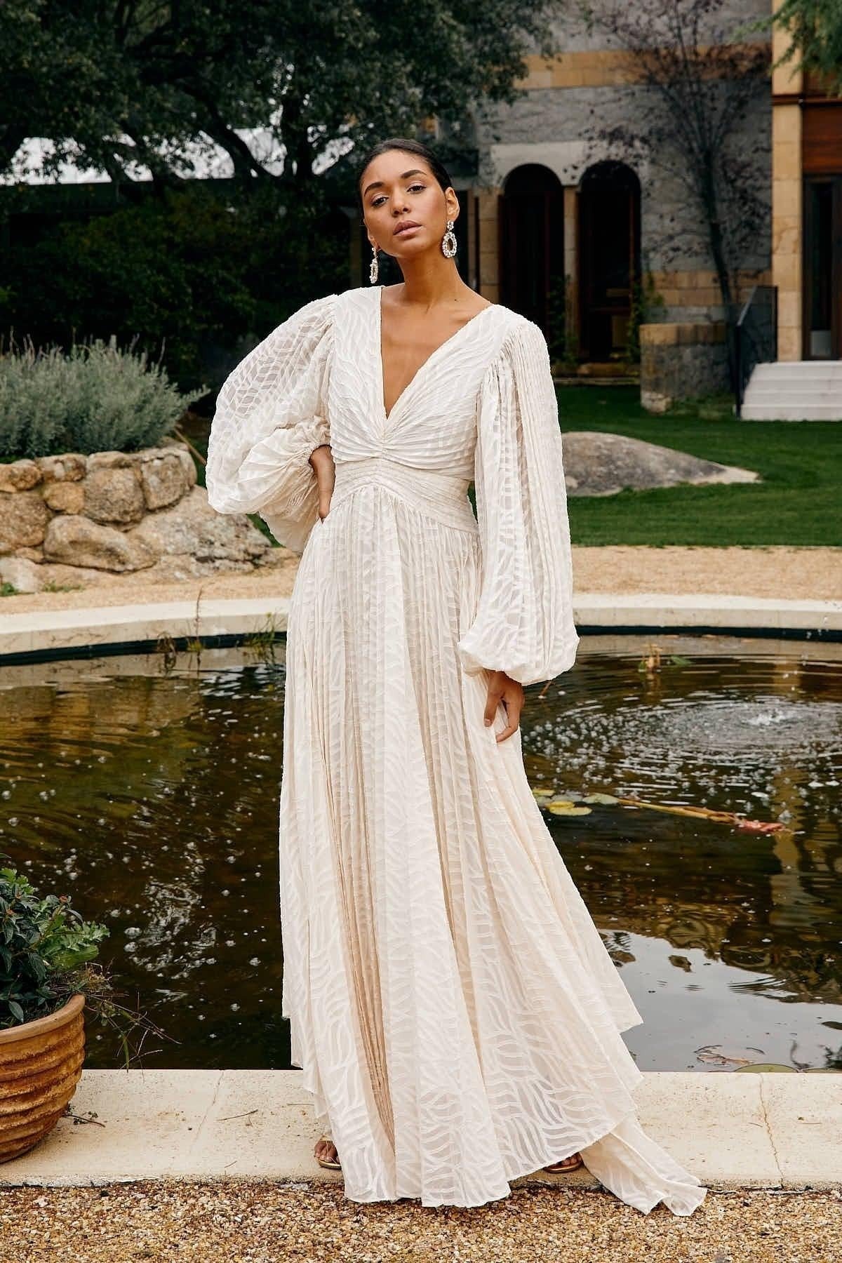 Woman in a white dress standing by a fountain with greenery in the background