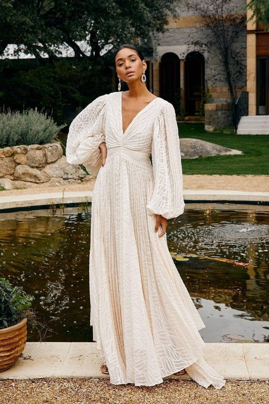 Woman in a white dress standing by a fountain with greenery in the background