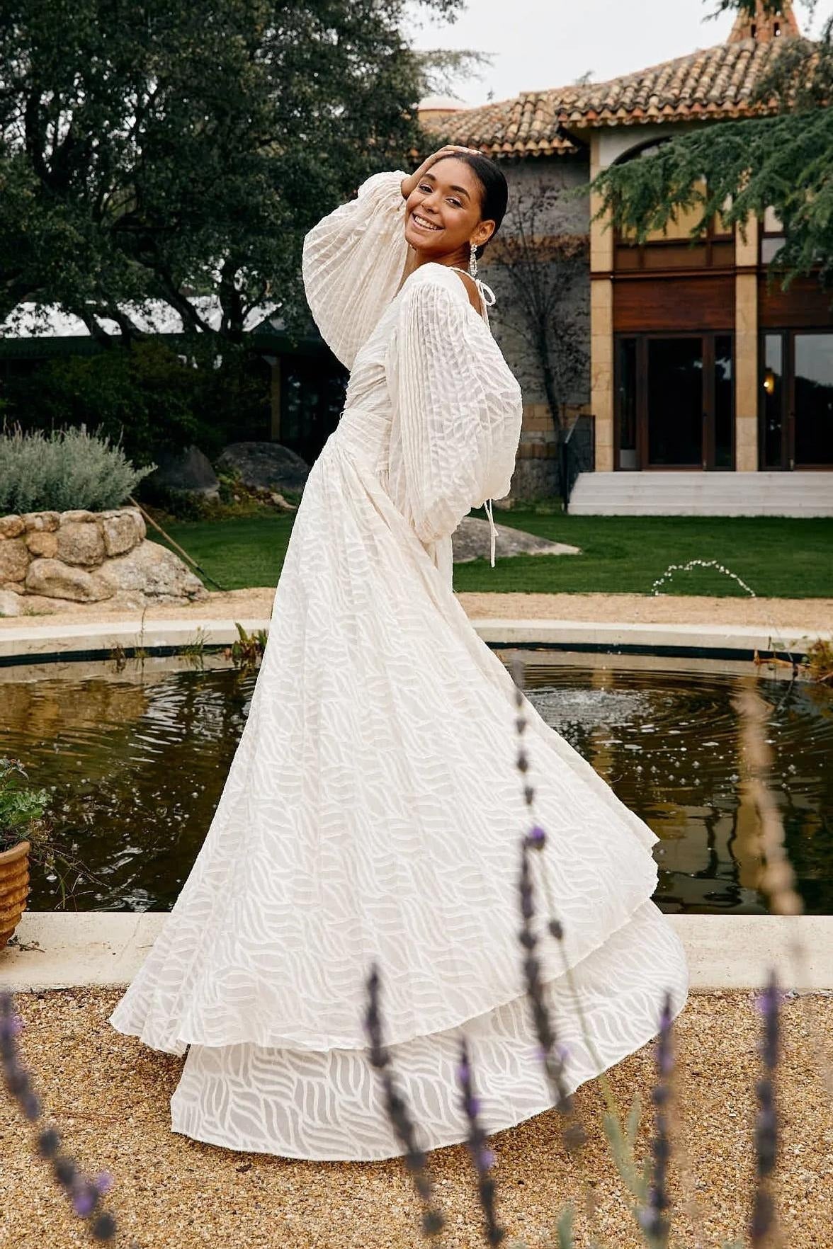 Woman in a white dress standing by a pond with a building in the background