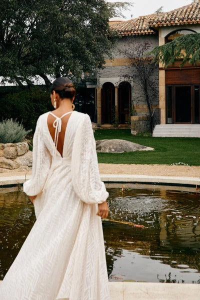 Woman in a white dress standing by a pond with a building and trees in the background