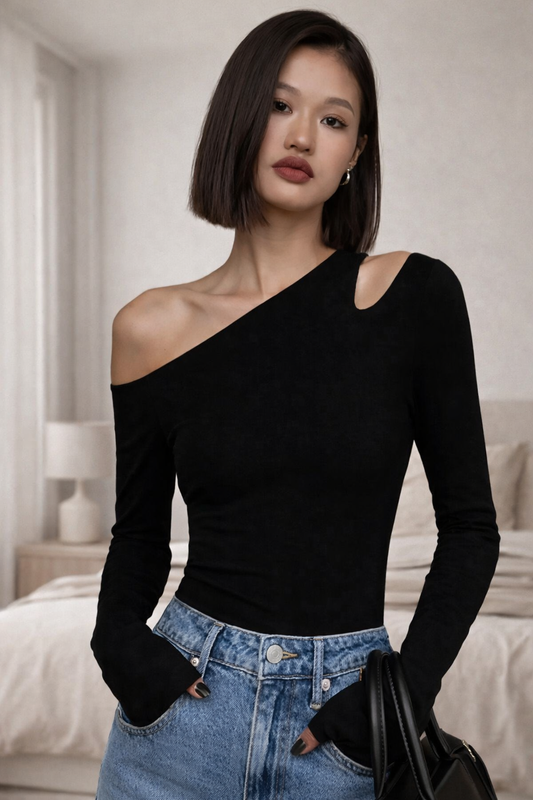 Woman wearing a black one-shoulder top and blue denim skirt in a bedroom setting.